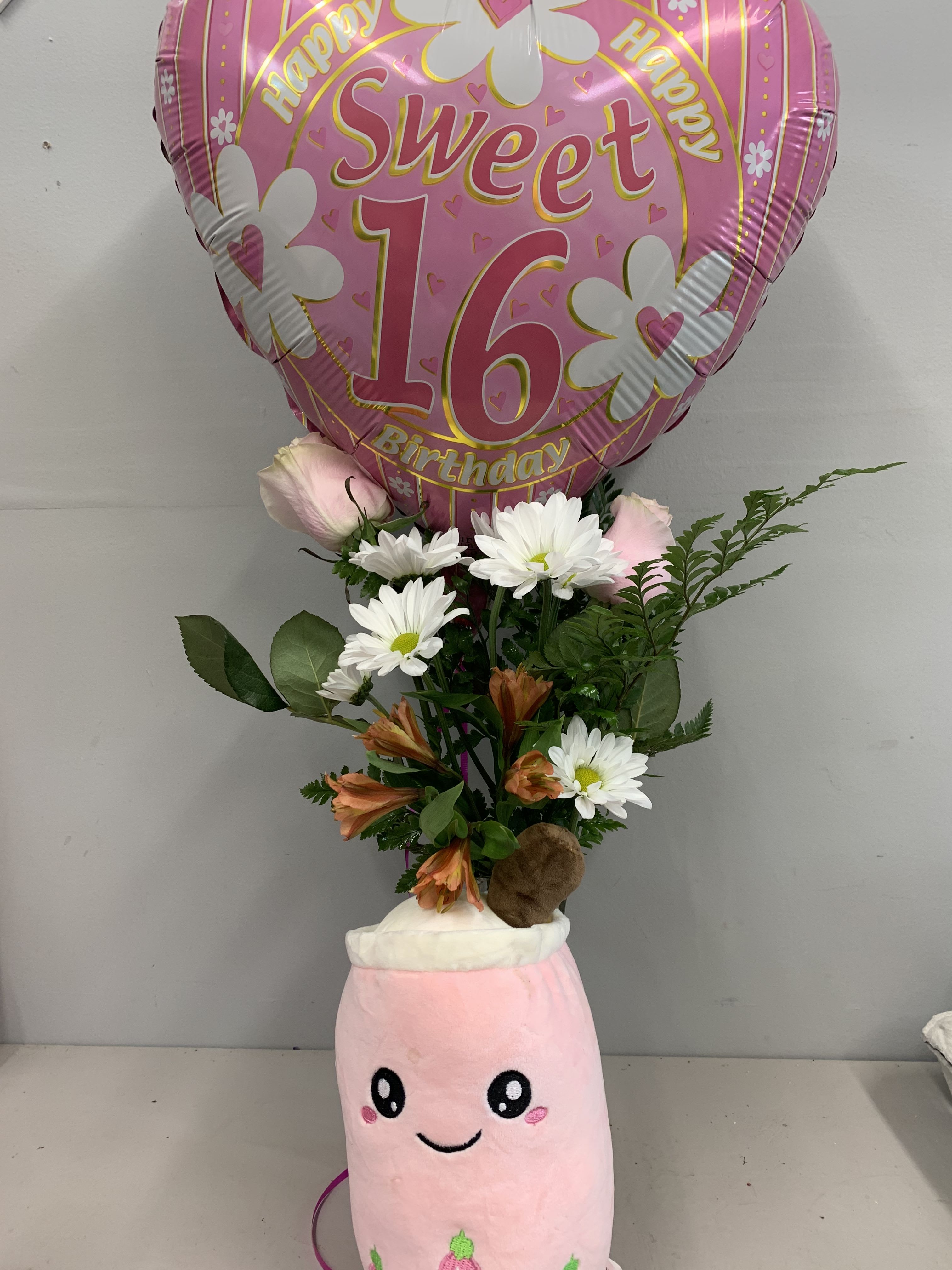 Pink birthday balloon above a small bouquet in a plush pink container