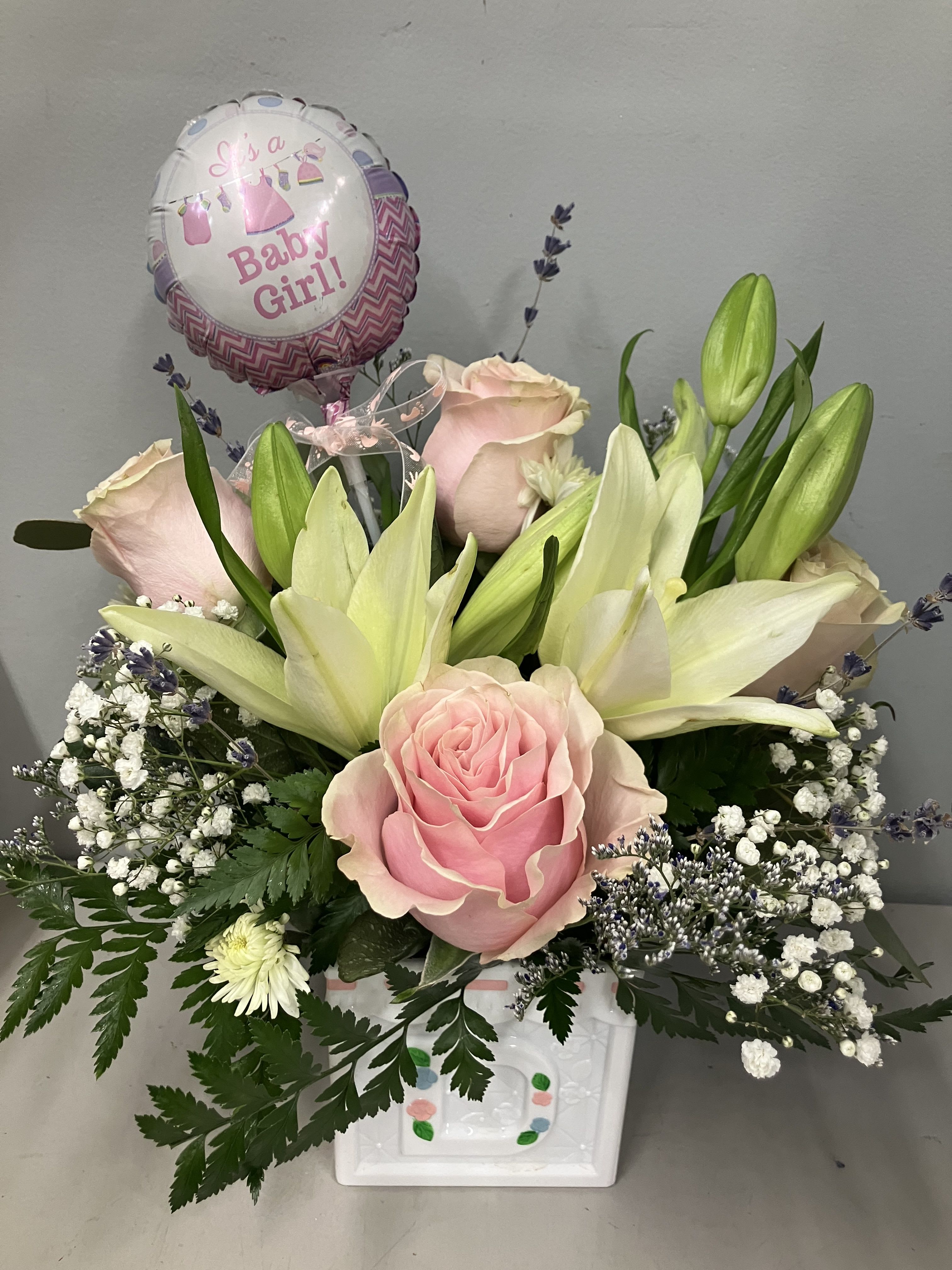 Baby Girl Arrangement  - Pretty white lily, baby skin soft pink roses, lavender and baby’s breath flowers for a new baby girl in a fun baby block container with footprint ribbon and mini balloon to celebrate your new arrival 