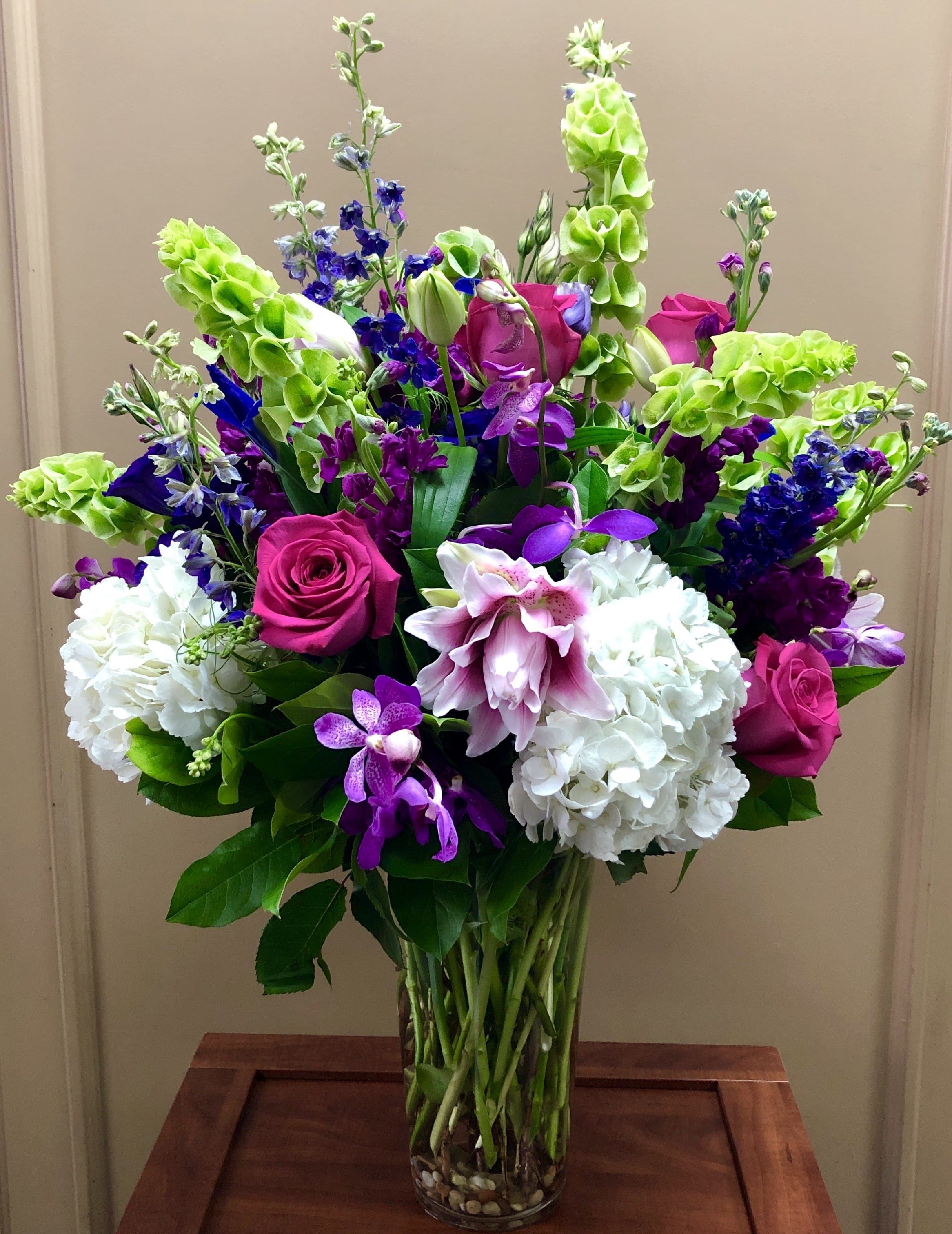 Tall mixed bouquet with pink roses, white hydrangeas, and purple orchids in a glass vase