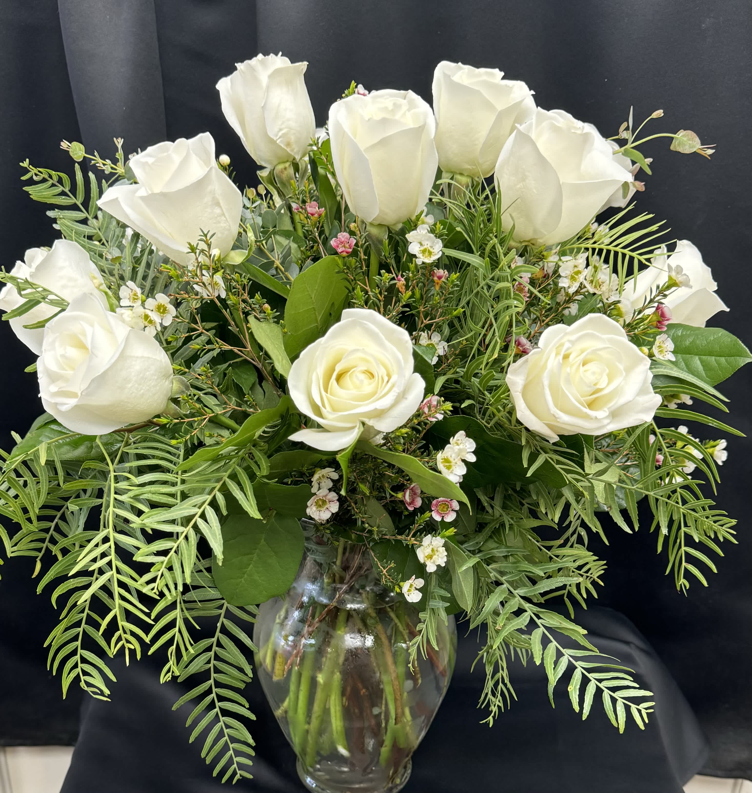 White roses arranged in a clear glass vase with mixed greenery