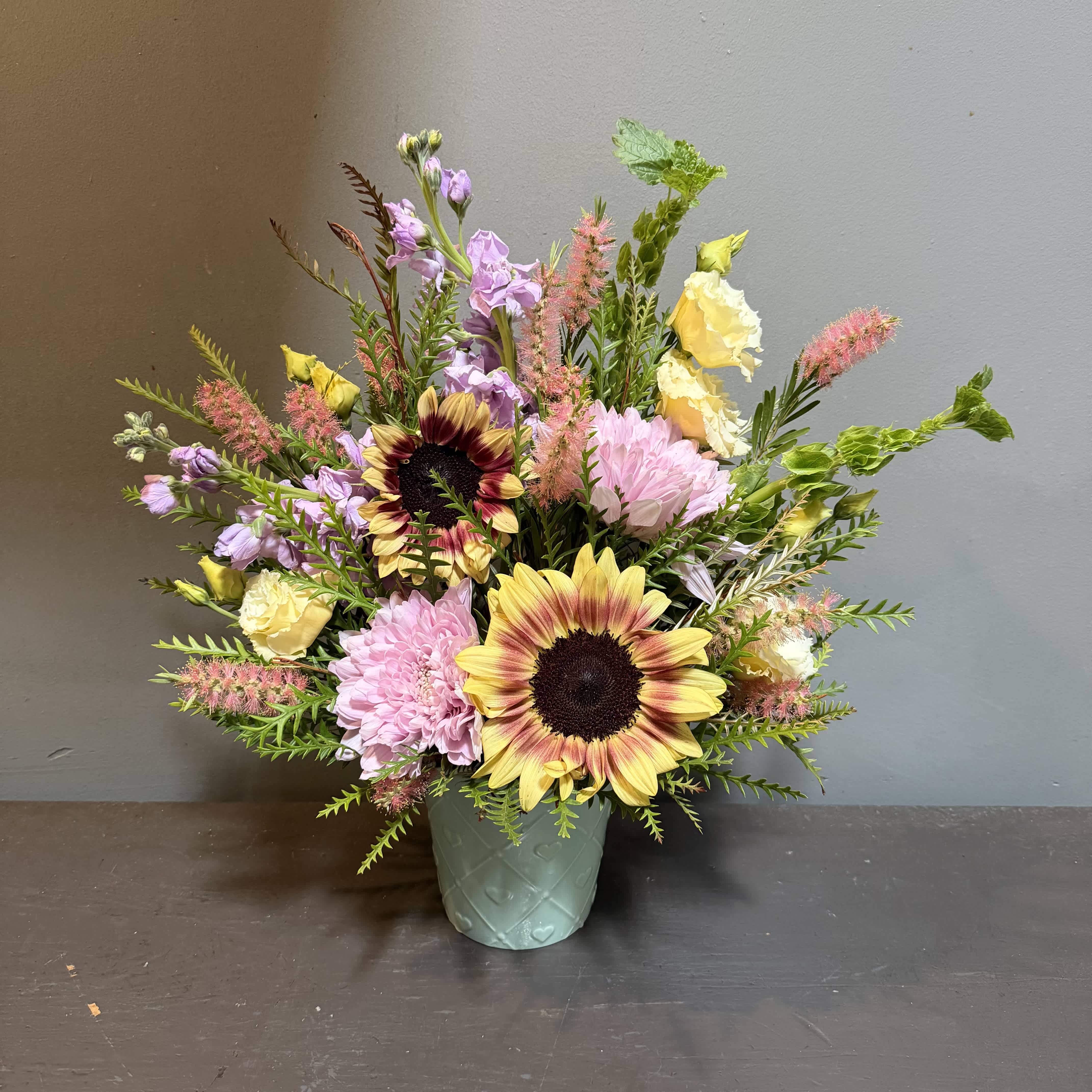 Mixed bouquet with sunflowers, pink blooms, and yellow flowers in a mint vase