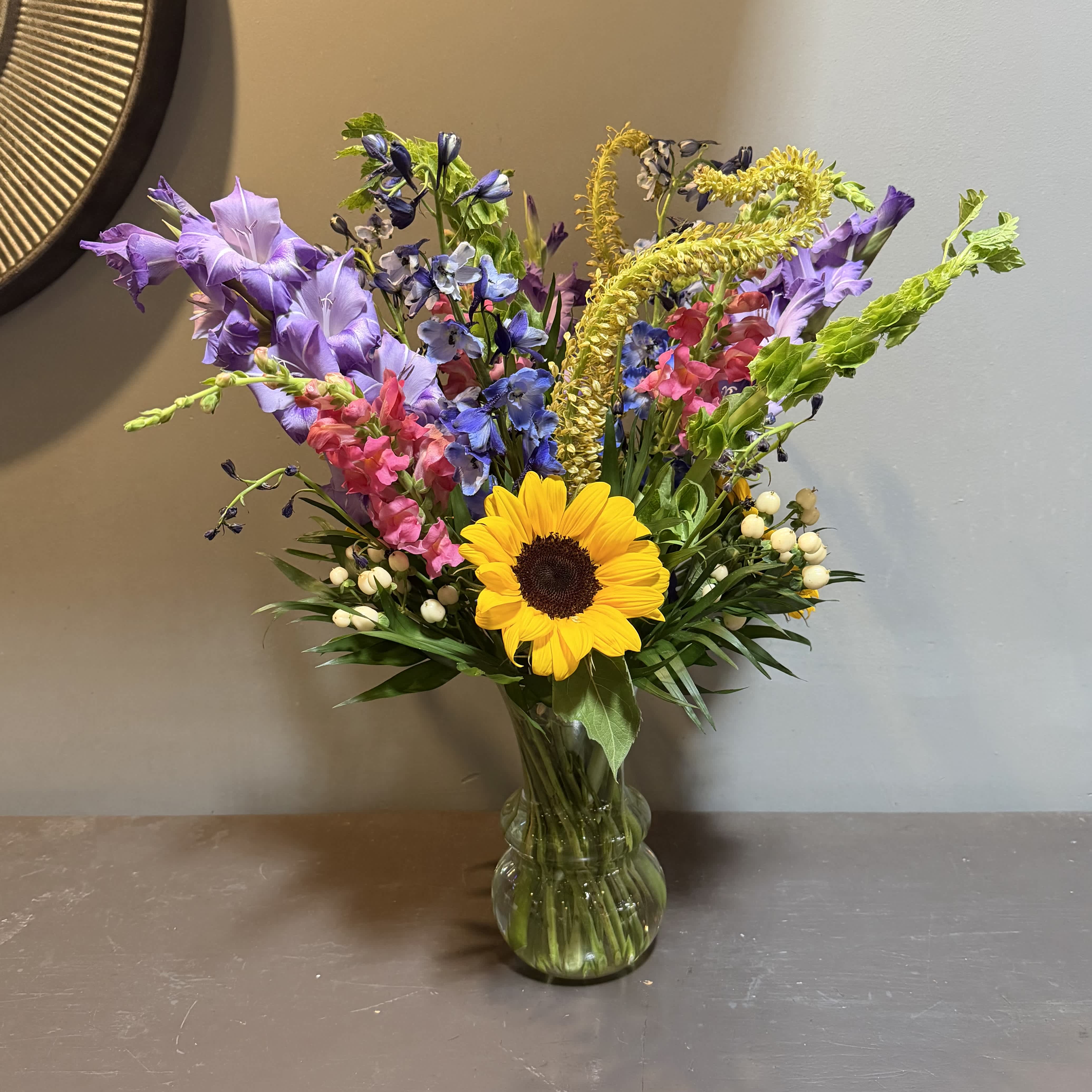 Mixed bouquet with a sunflower and purple, pink, and blue flowers in a glass vase