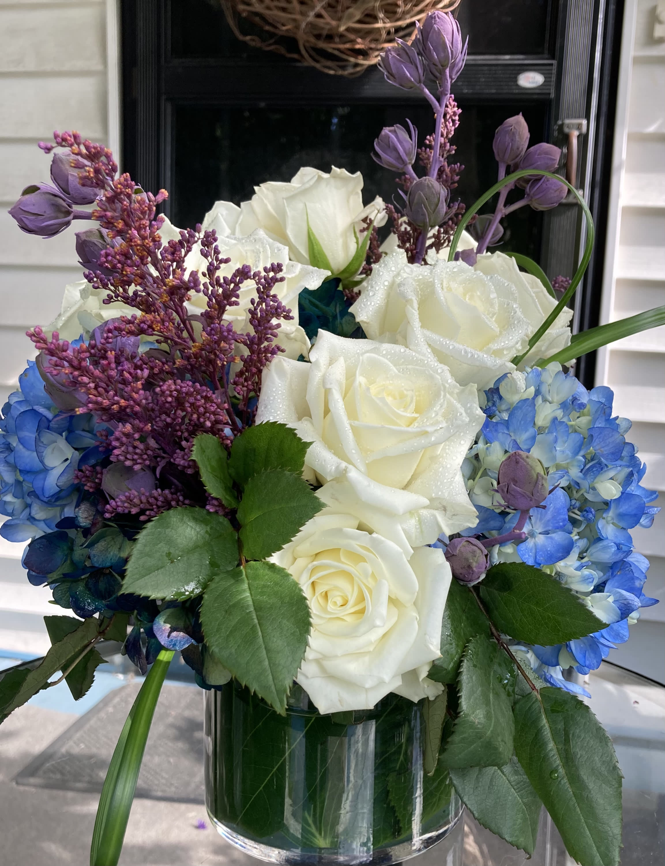 White roses and blue hydrangeas in a glass vase with purple accents