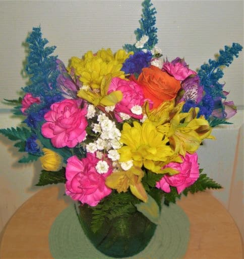 Bright mixed bouquet in a green vase with pink, yellow, orange, and blue flowers
