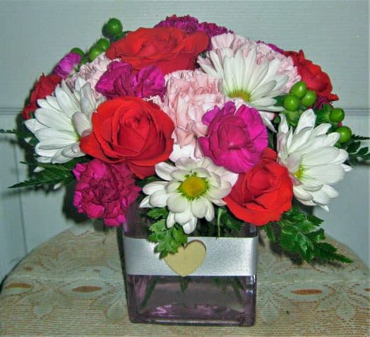 Bouquet of red roses, white daisies, and pink carnations in a square vase