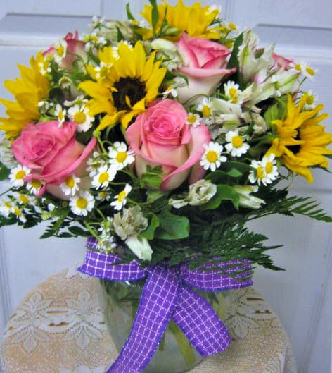 Bouquet of pink roses, sunflowers, and white daisies with a purple ribbon