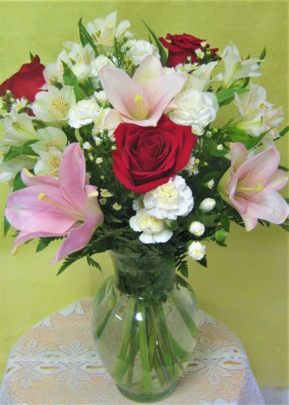 Bouquet of red roses, pink lilies, and white flowers in a glass vase