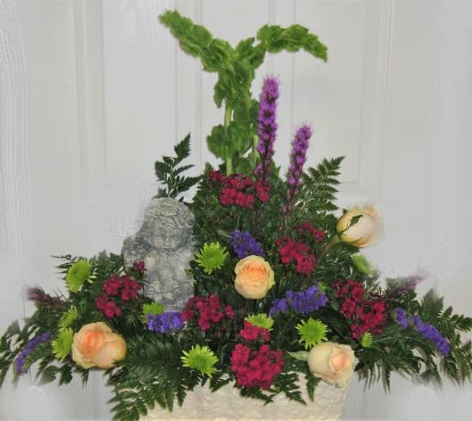 Mixed floral arrangement with peach roses, purple blooms, and a small angel statue