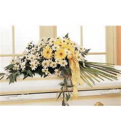 White and yellow daisy arrangement on a casket with a yellow ribbon