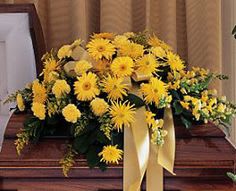 Yellow floral casket spray with a cream ribbon
