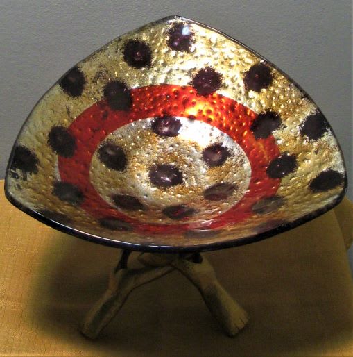 Decorative metallic bowl with red and black spotted pattern on a stand