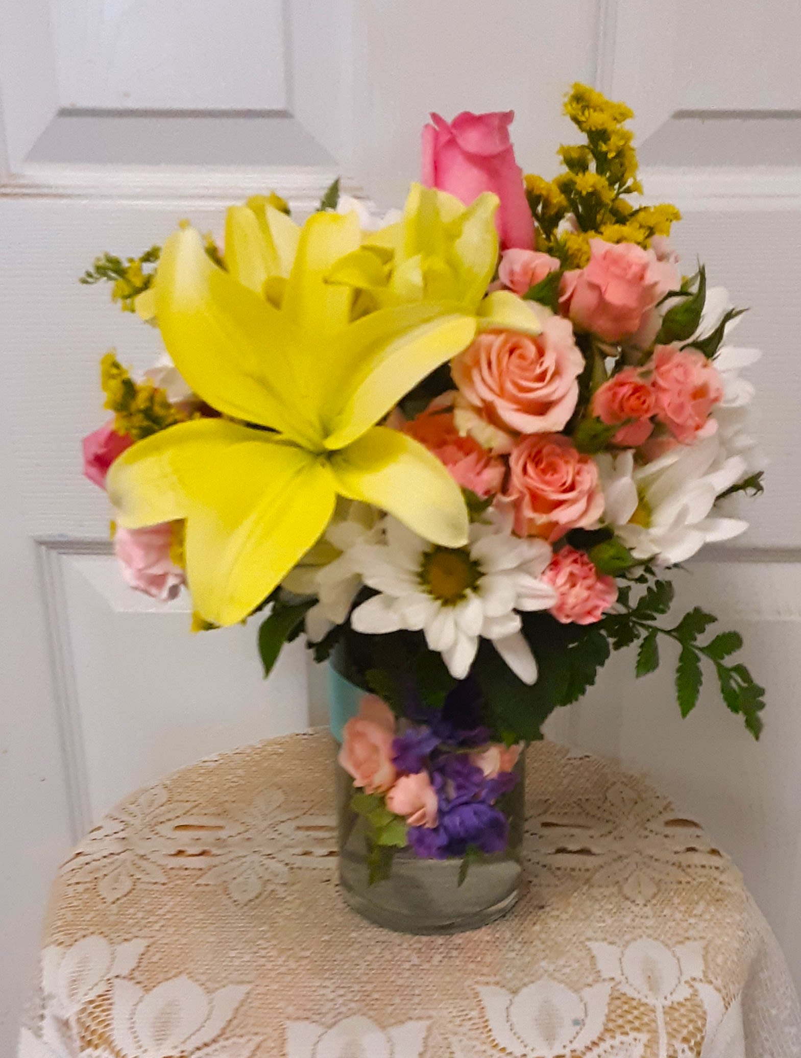 Bouquet of yellow lilies, pink roses, and white daisies in a glass vase