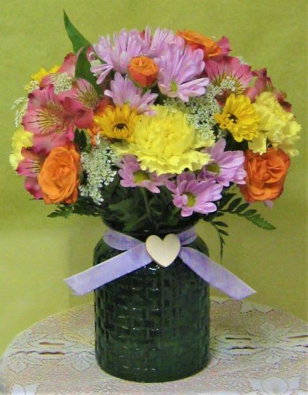 Mixed bouquet of pink, yellow, and orange flowers in a dark vase with a ribbon