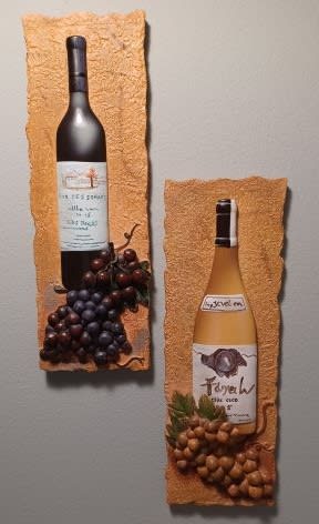 Two wine bottles mounted on textured wall plaques with grape clusters