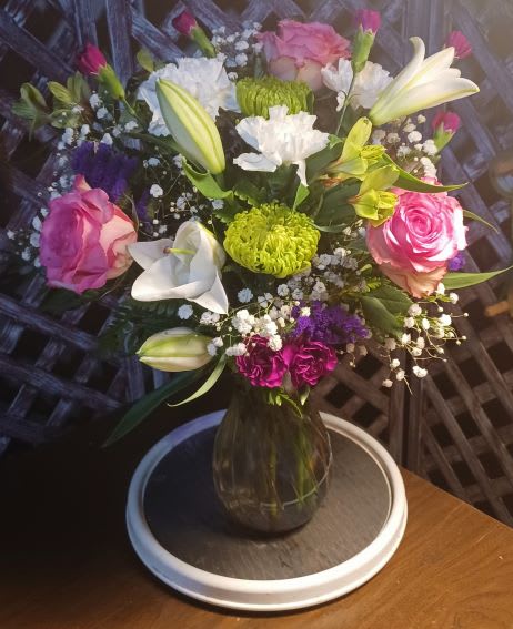Mixed bouquet of pink roses, white lilies, and chrysanthemums in a glass vase
