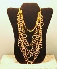 Layered gold-toned necklace displayed on a black bust stand
