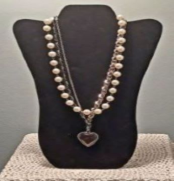 Two pearl necklaces on a black display bust with a heart pendant
