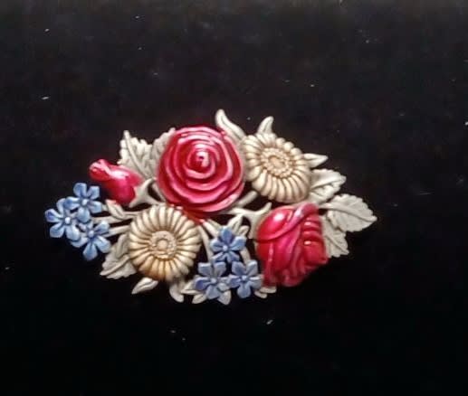 Decorative floral brooch with red, cream, and blue flowers on a black background