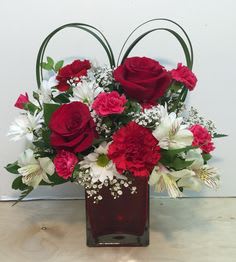 Red roses and carnations in a square glass vase with looped handles