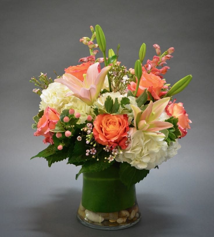 Bouquet of orange roses, lilies, and white hydrangeas in a glass vase