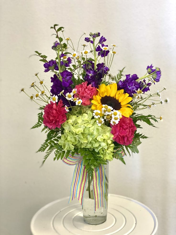 Colorful mixed bouquet in a clear glass vase with a striped ribbon