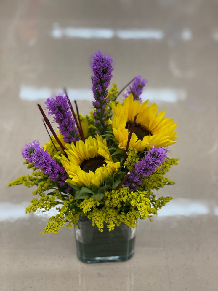 Sunflowers and purple flowers arranged in a square glass vase