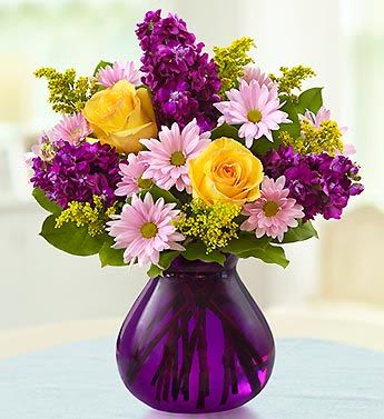 Yellow roses and pink daisies in a purple glass vase