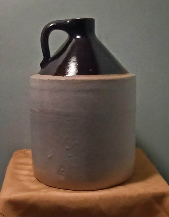 Dark ceramic jug in a beige sleeve on a wooden surface