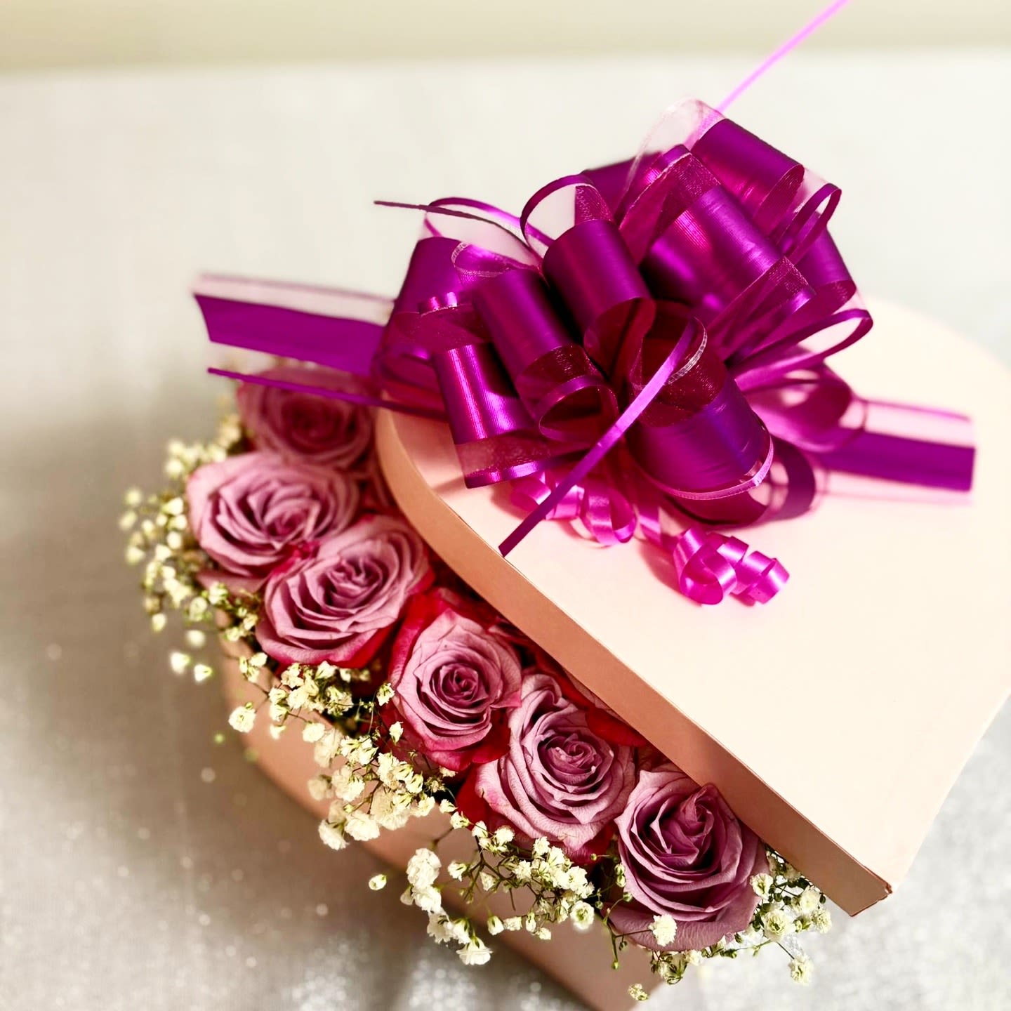Heart-shaped box of pink roses with a purple ribbon bow