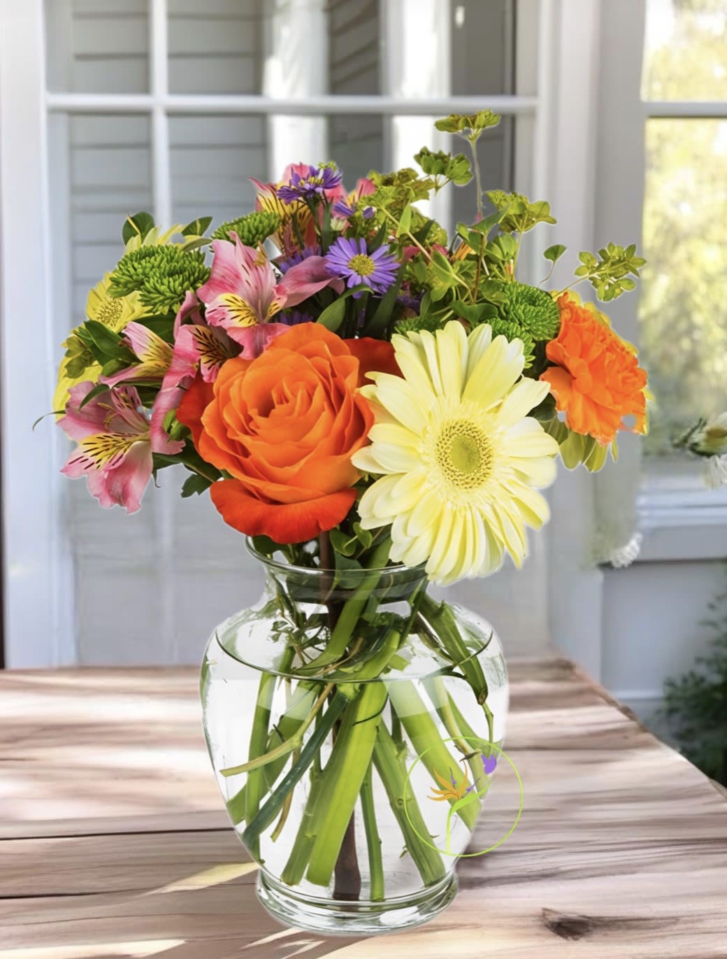 Mixed bouquet of orange, yellow, pink, and purple flowers in a clear glass vase.
