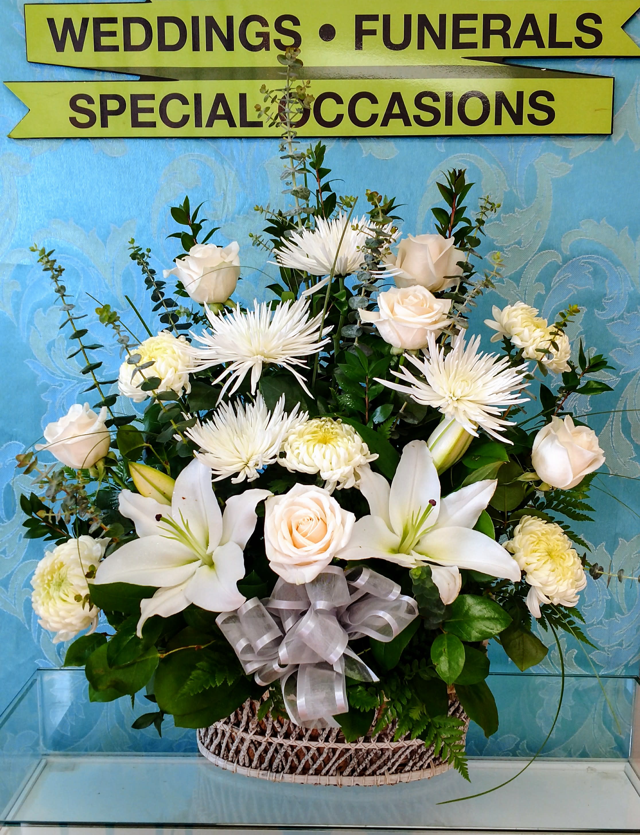 White floral arrangement in a woven basket with a silver ribbon