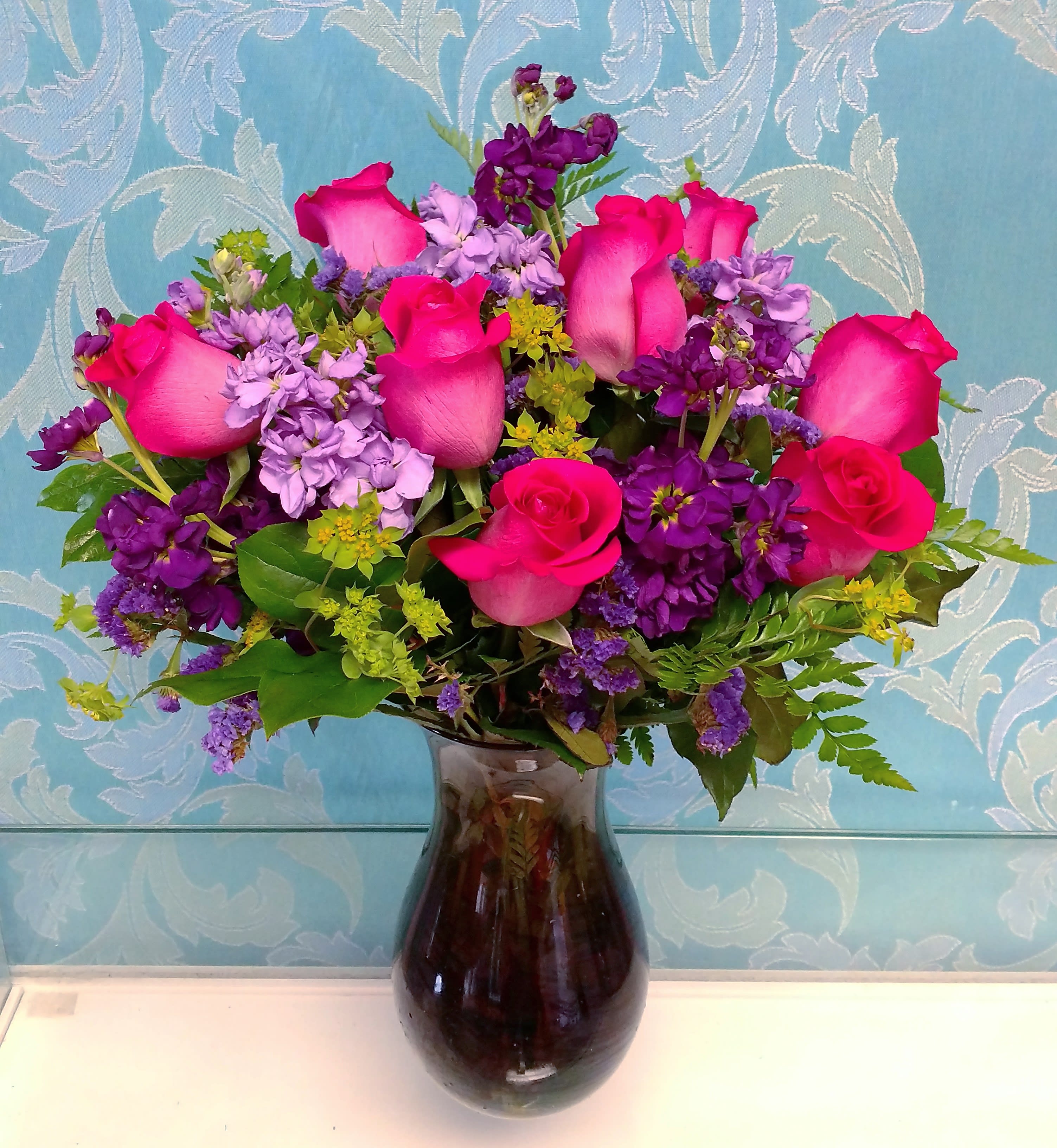 Pink roses and purple flowers arranged in a dark glass vase