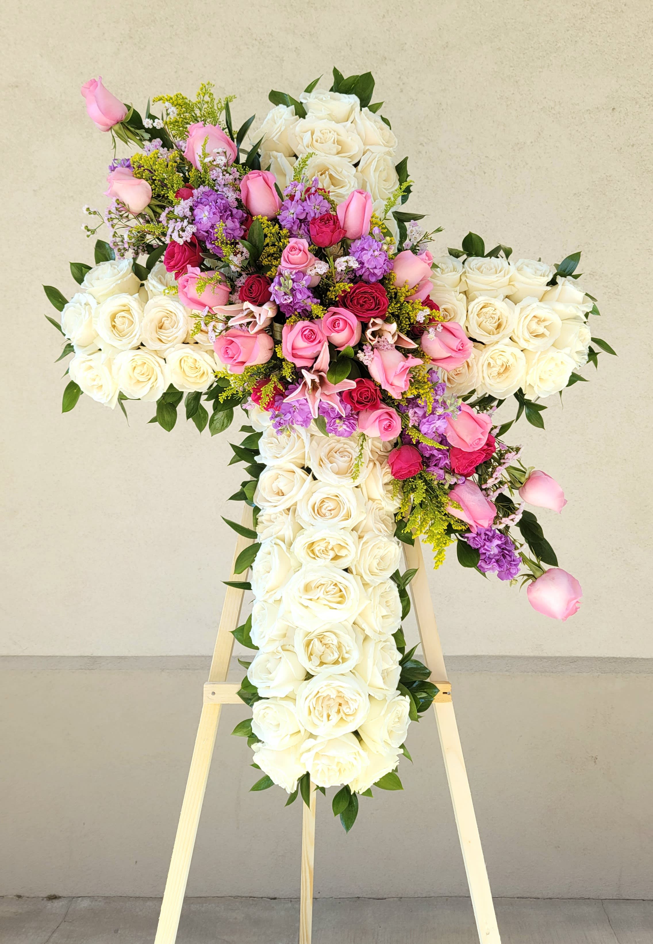 Large cross-shaped floral arrangement of white, pink, and purple roses on an easel