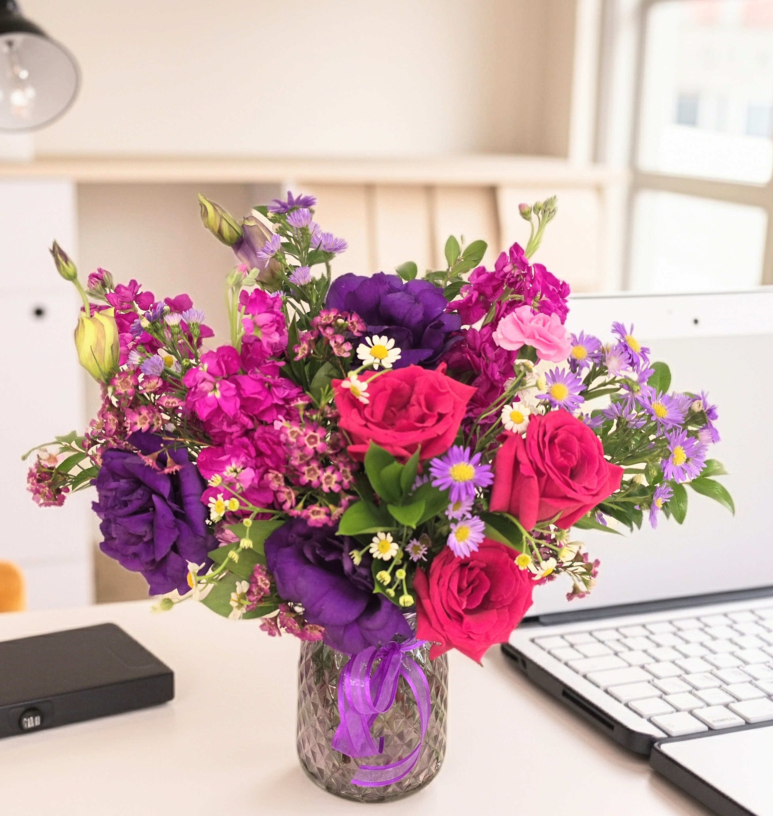 Bright mixed bouquet of pink, purple, and white flowers in a glass vase