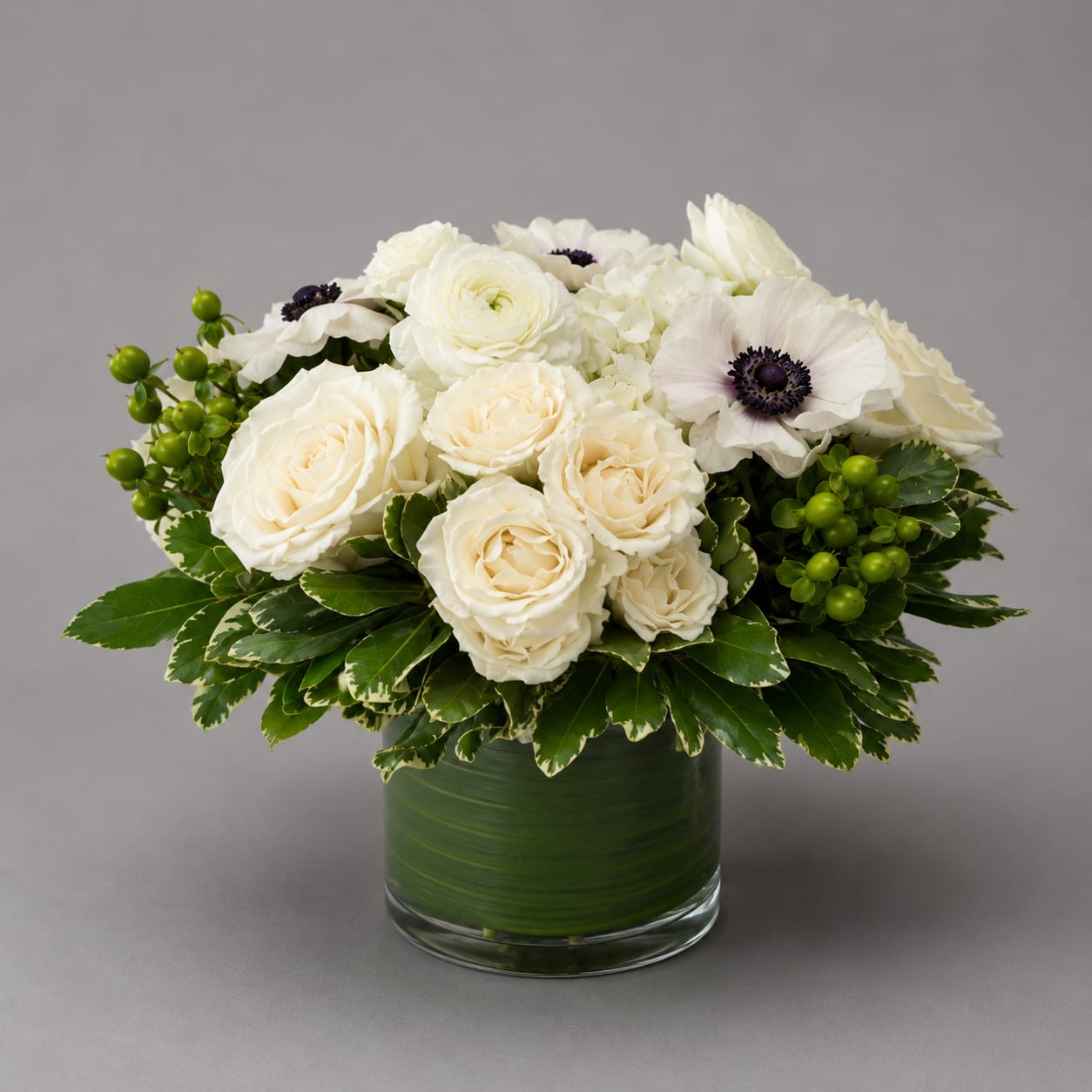 White roses and anemones arranged in a glass vase with green berries