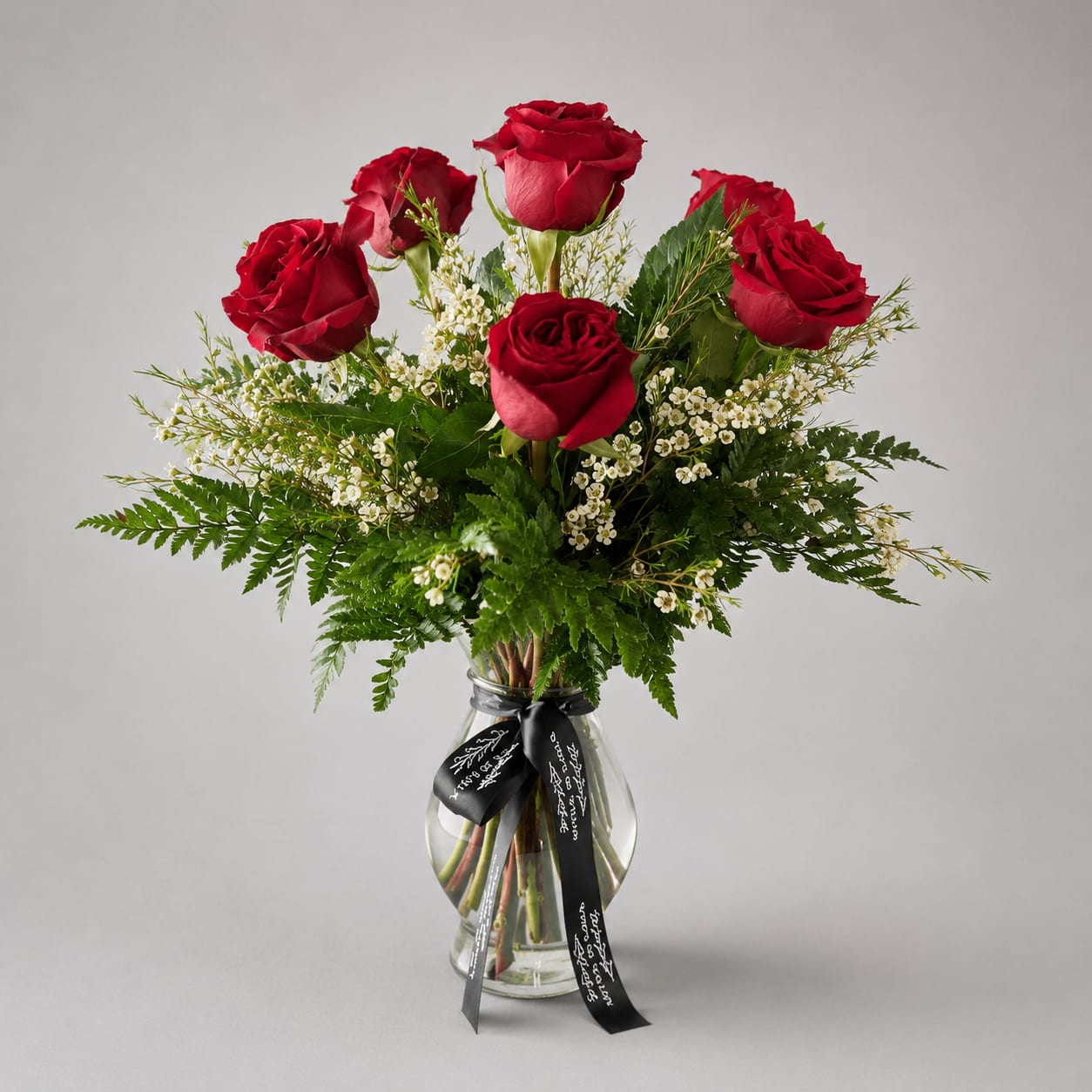 Red roses arranged in a clear glass vase with white filler flowers.
