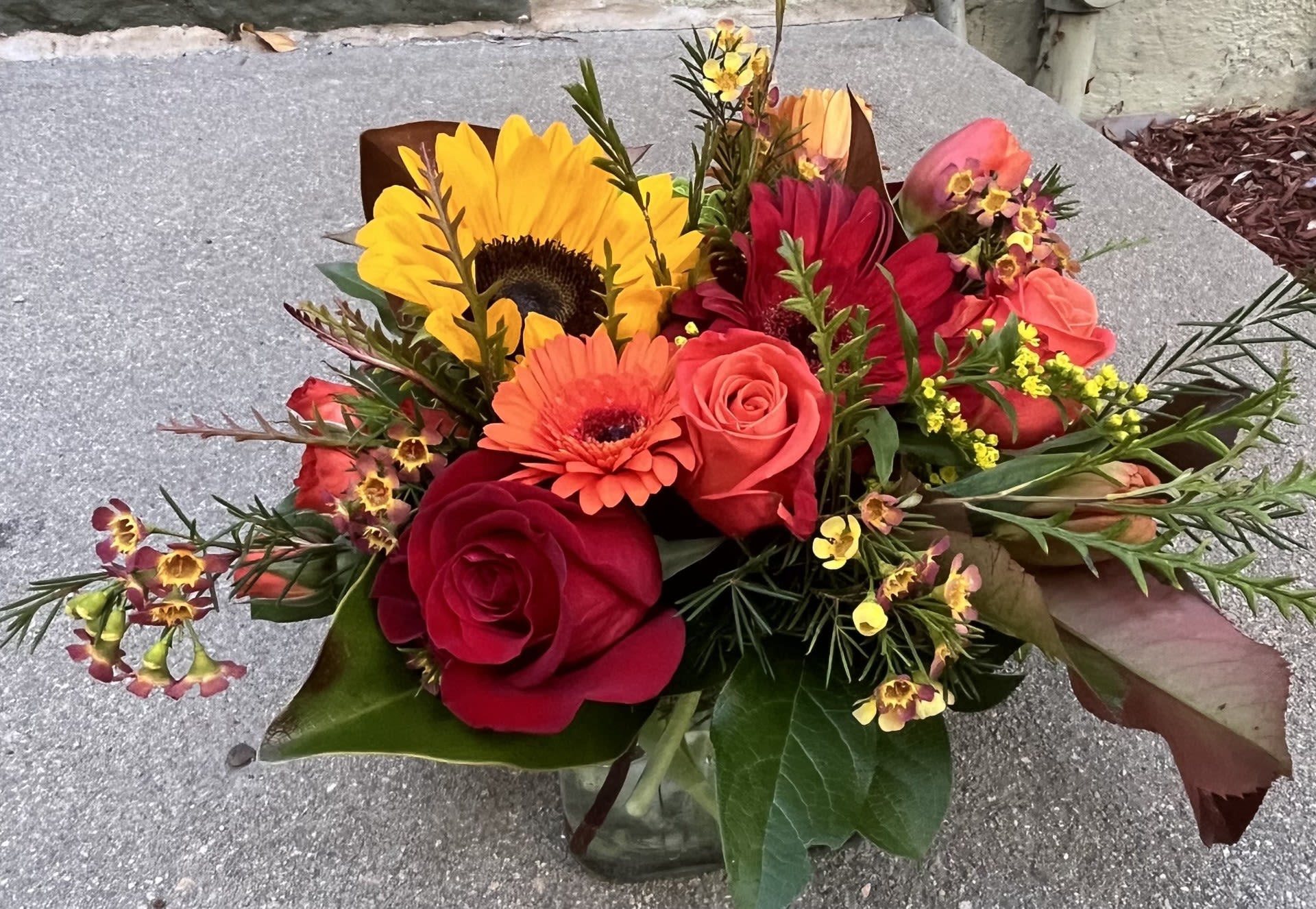 Bouquet of sunflowers, roses, and gerbera daisies in a glass vase