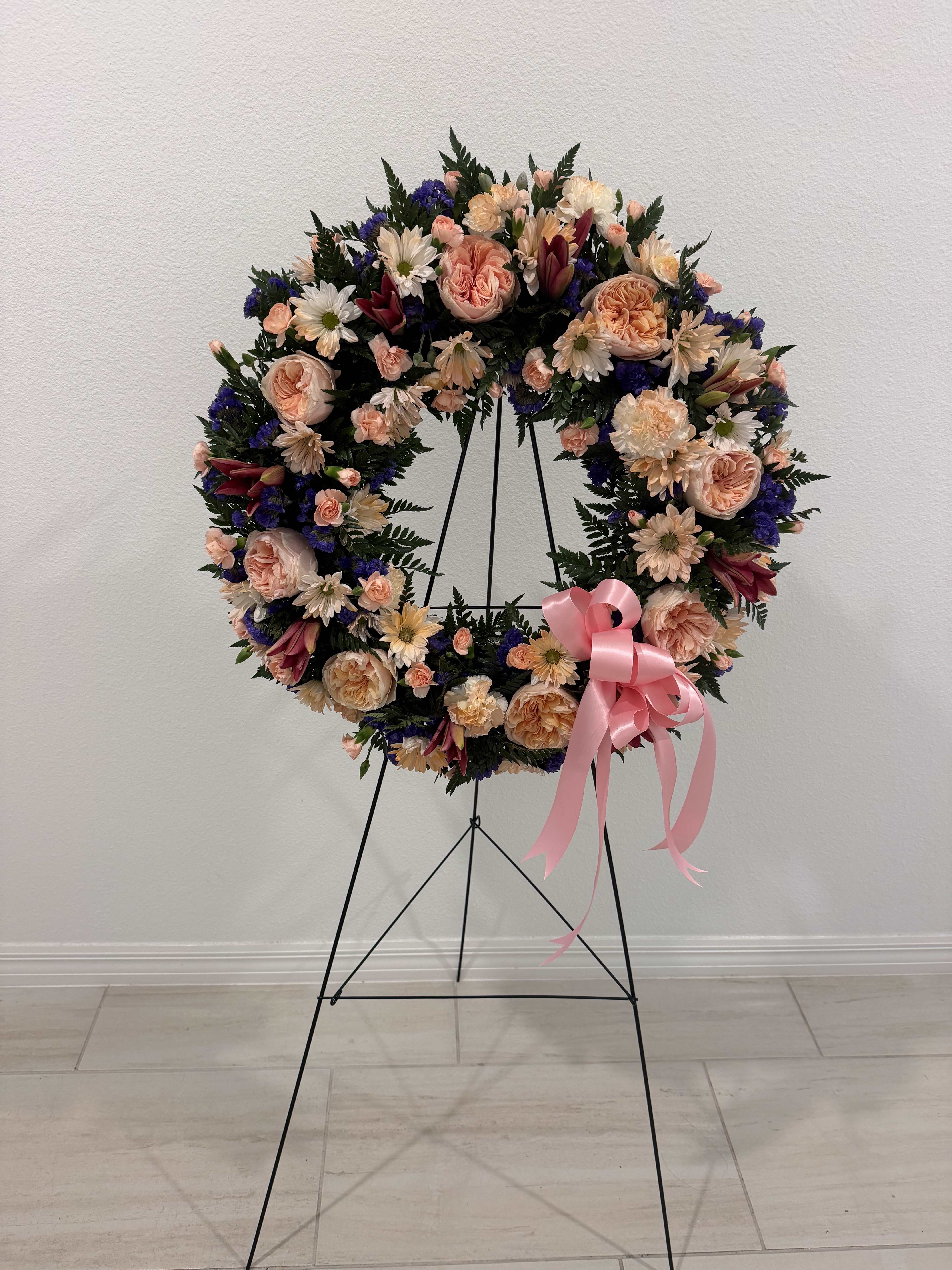 Large floral wreath on a black stand with a pink ribbon bow