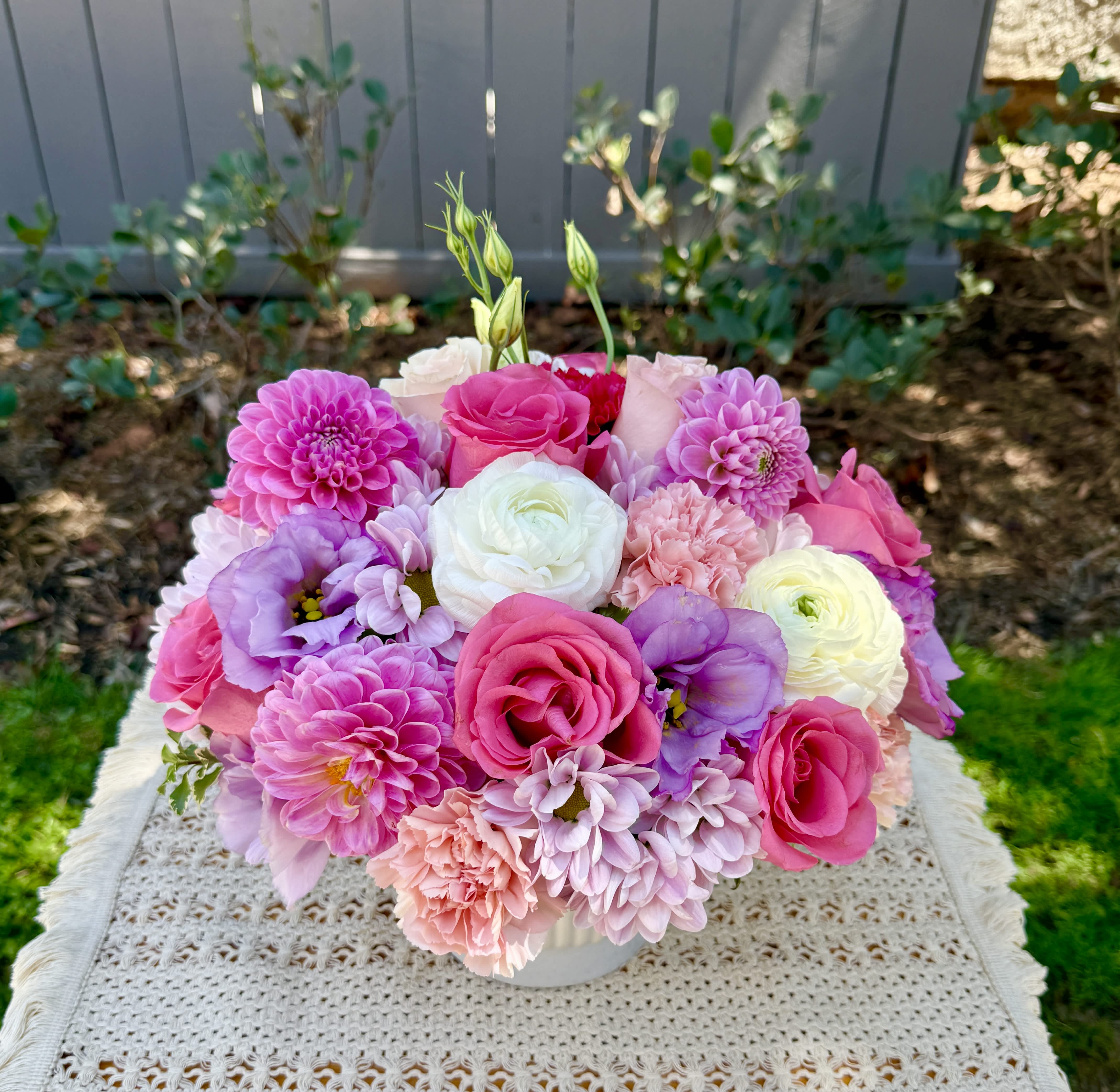 Pink, purple, and white flowers arranged in a low white vase