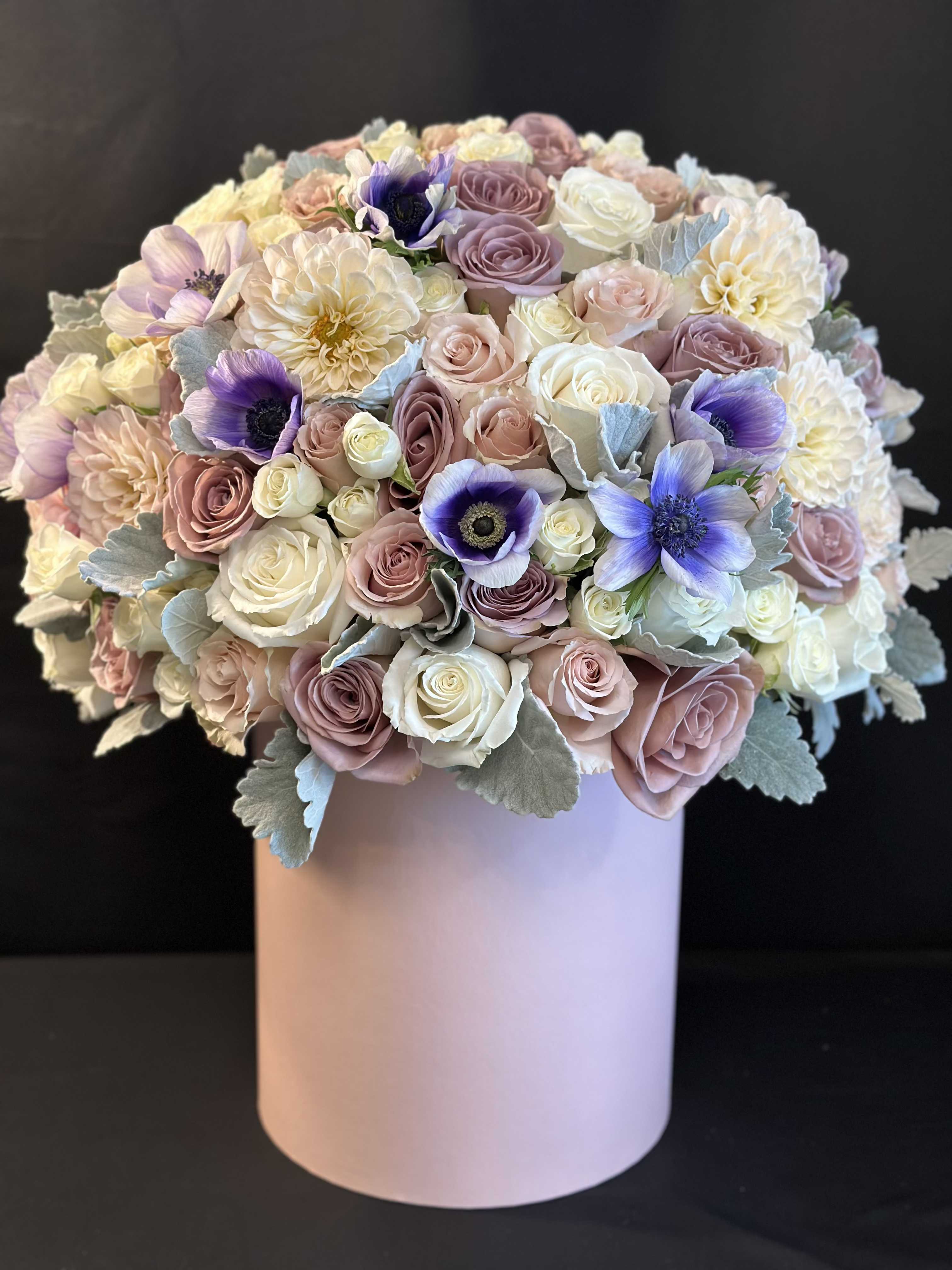 Round bouquet of pastel roses and purple flowers in a pink box