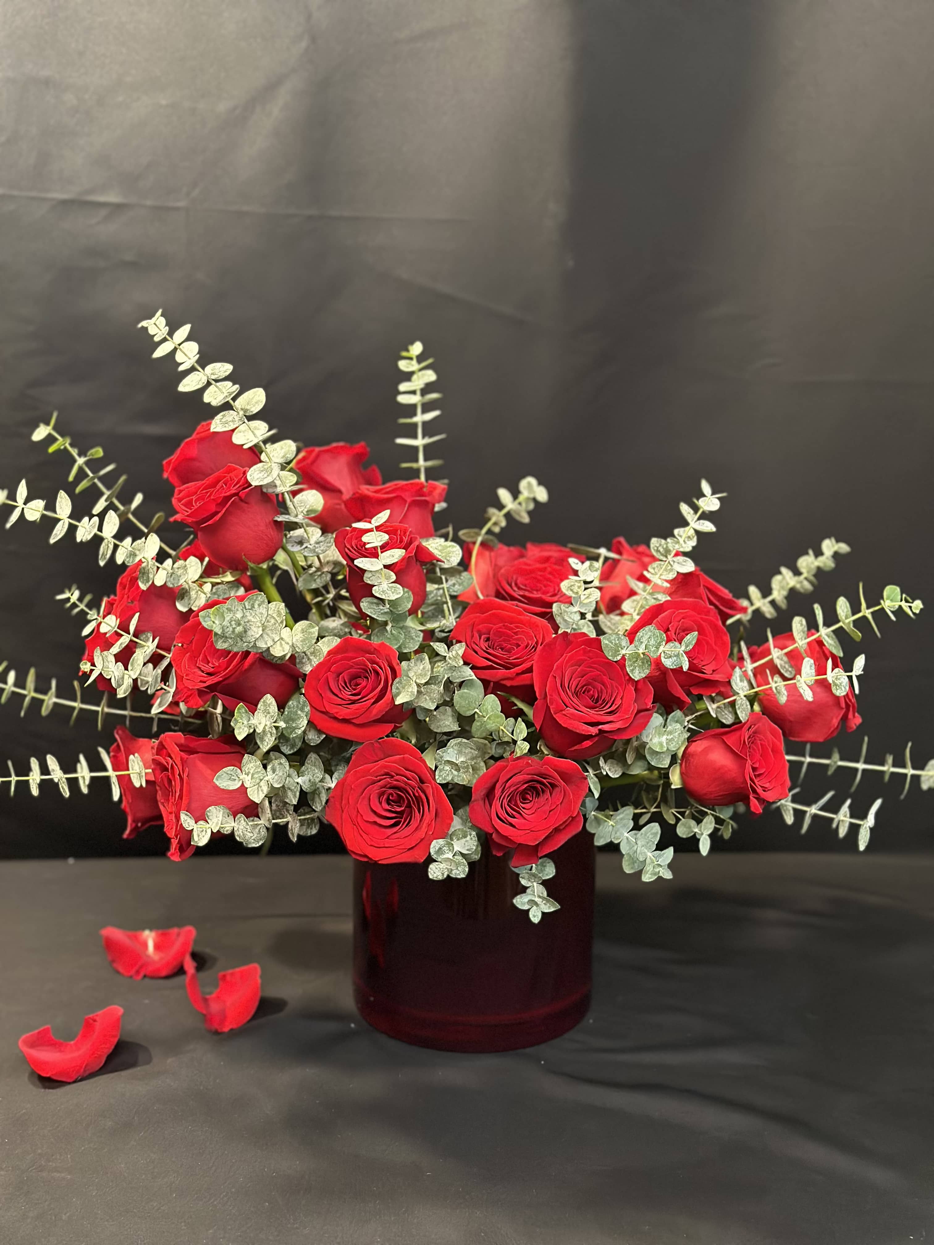 Red roses arranged in a dark glass vase with silver-green foliage