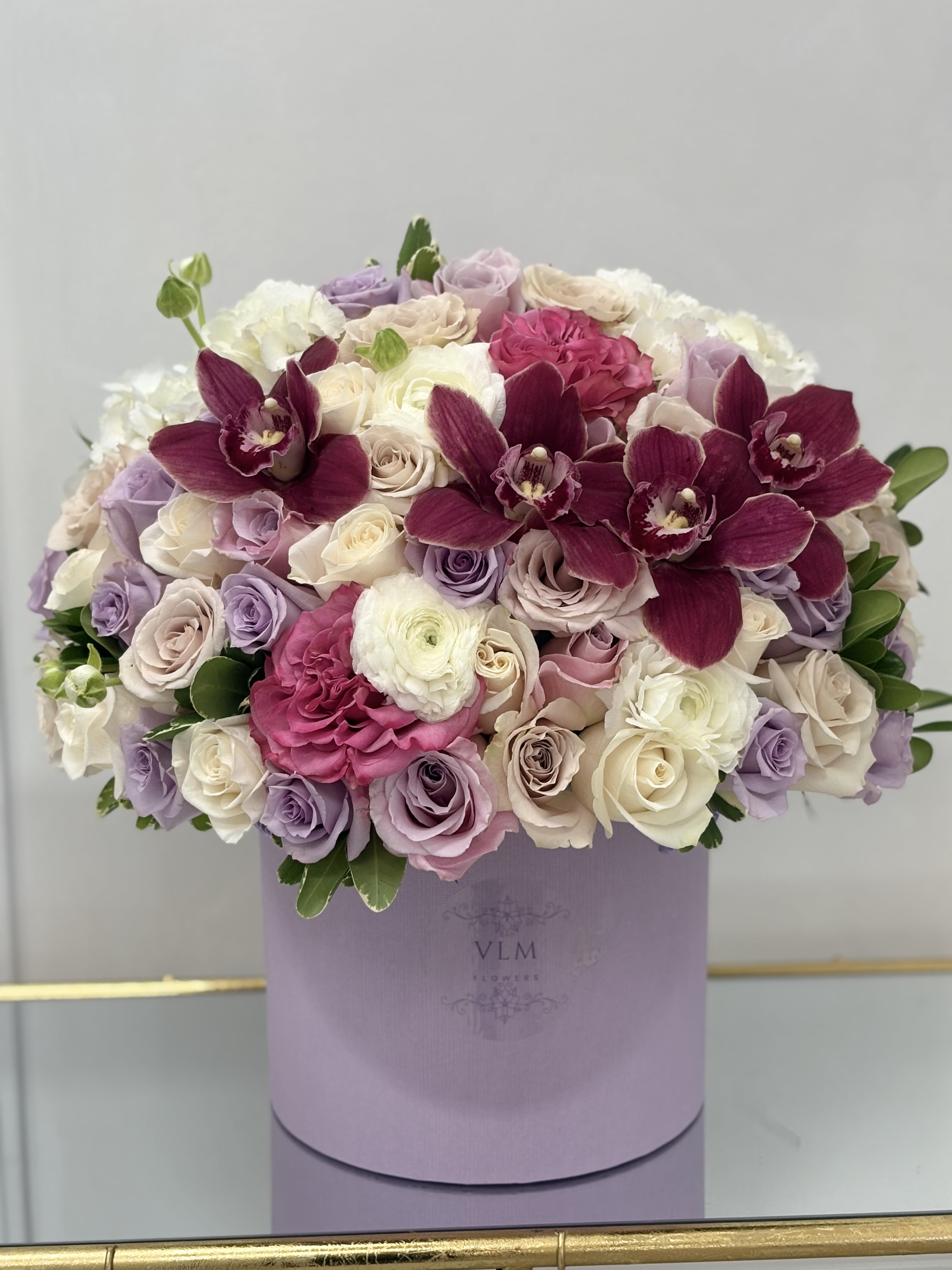 Lavender and white rose bouquet with deep magenta orchids in a round box