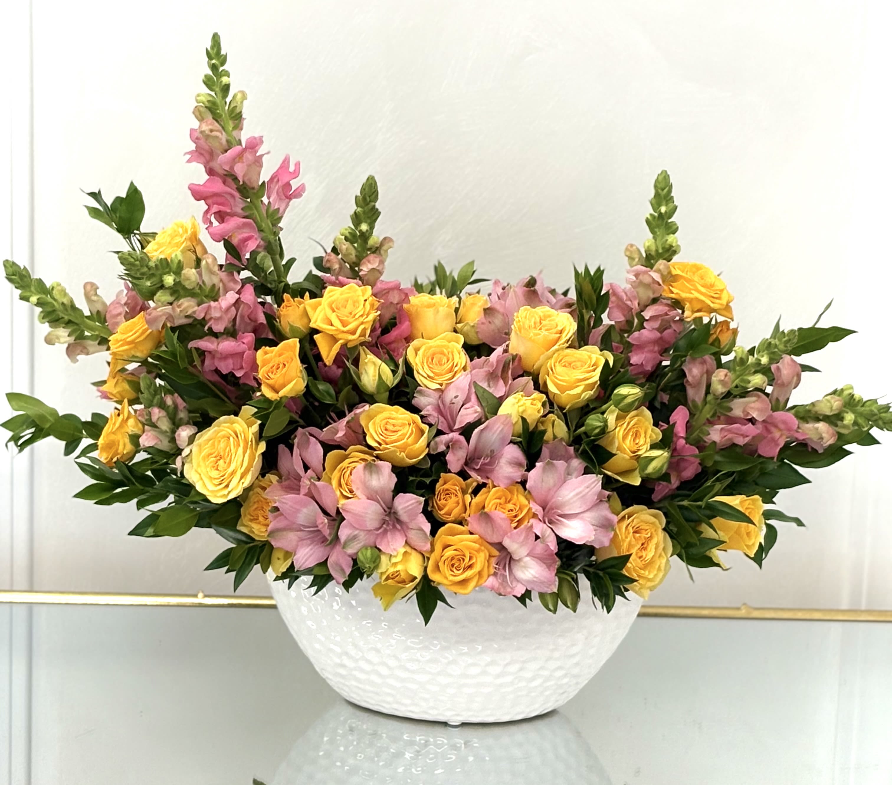 Yellow roses and pink snapdragons arranged in a white bowl vase