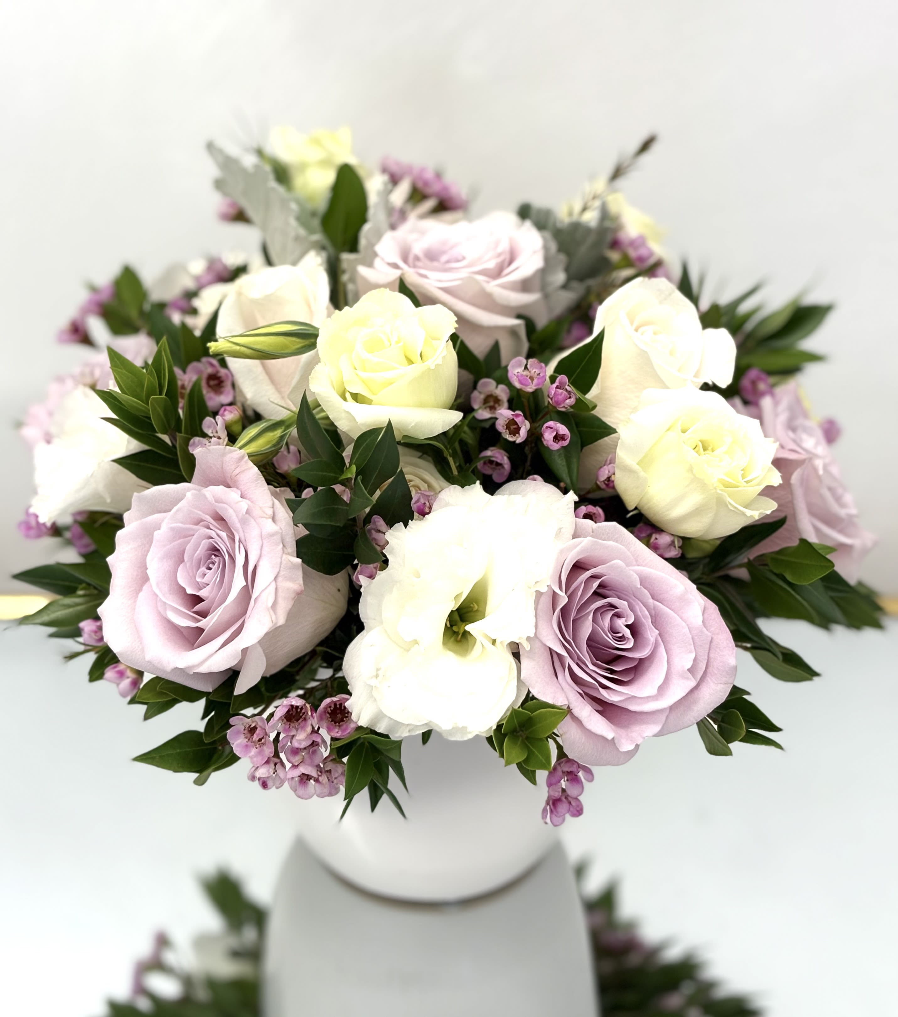 Pastel roses and white blooms arranged in a white vase