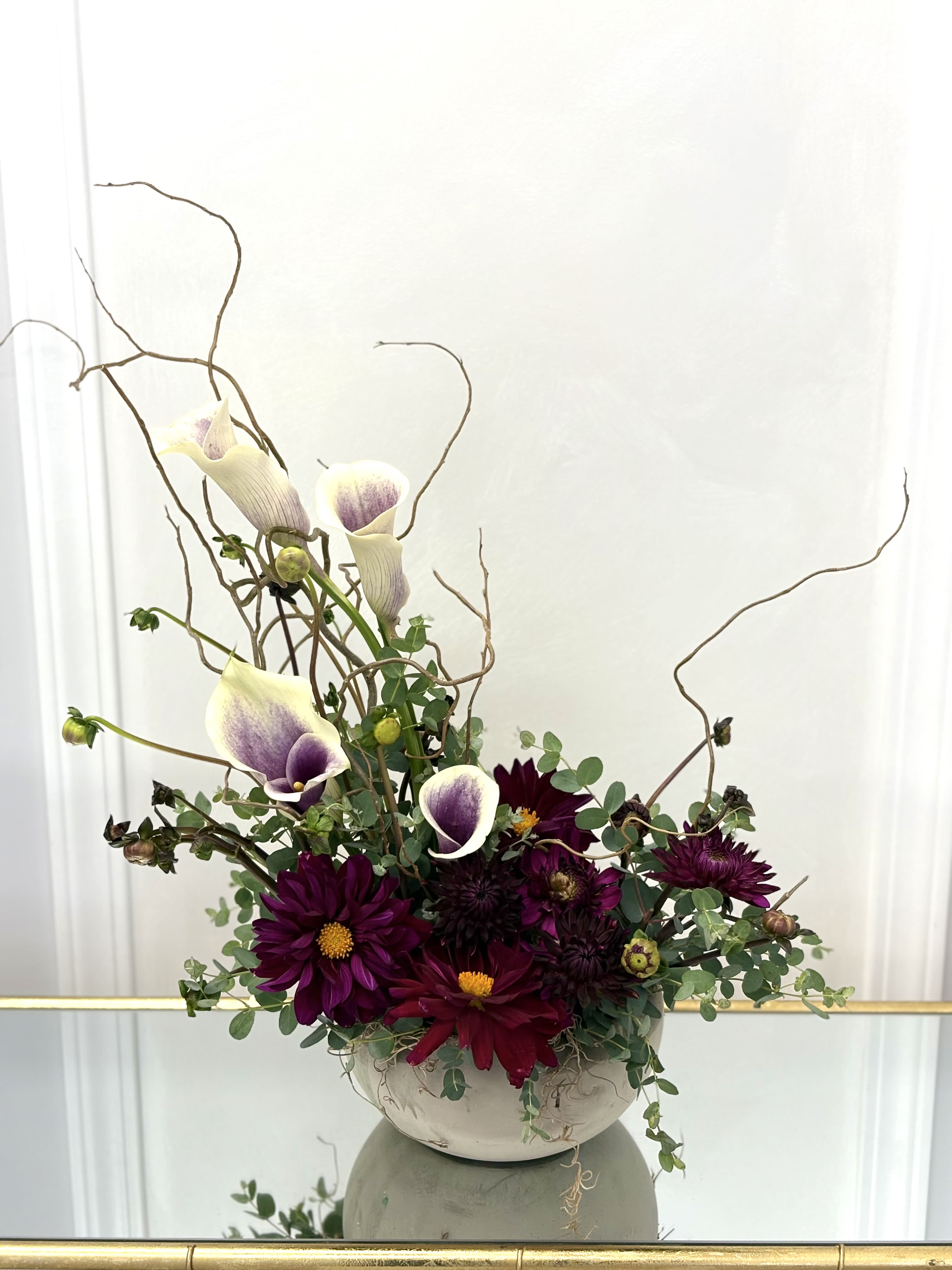 Purple calla lilies and dark dahlias in a white bowl vase