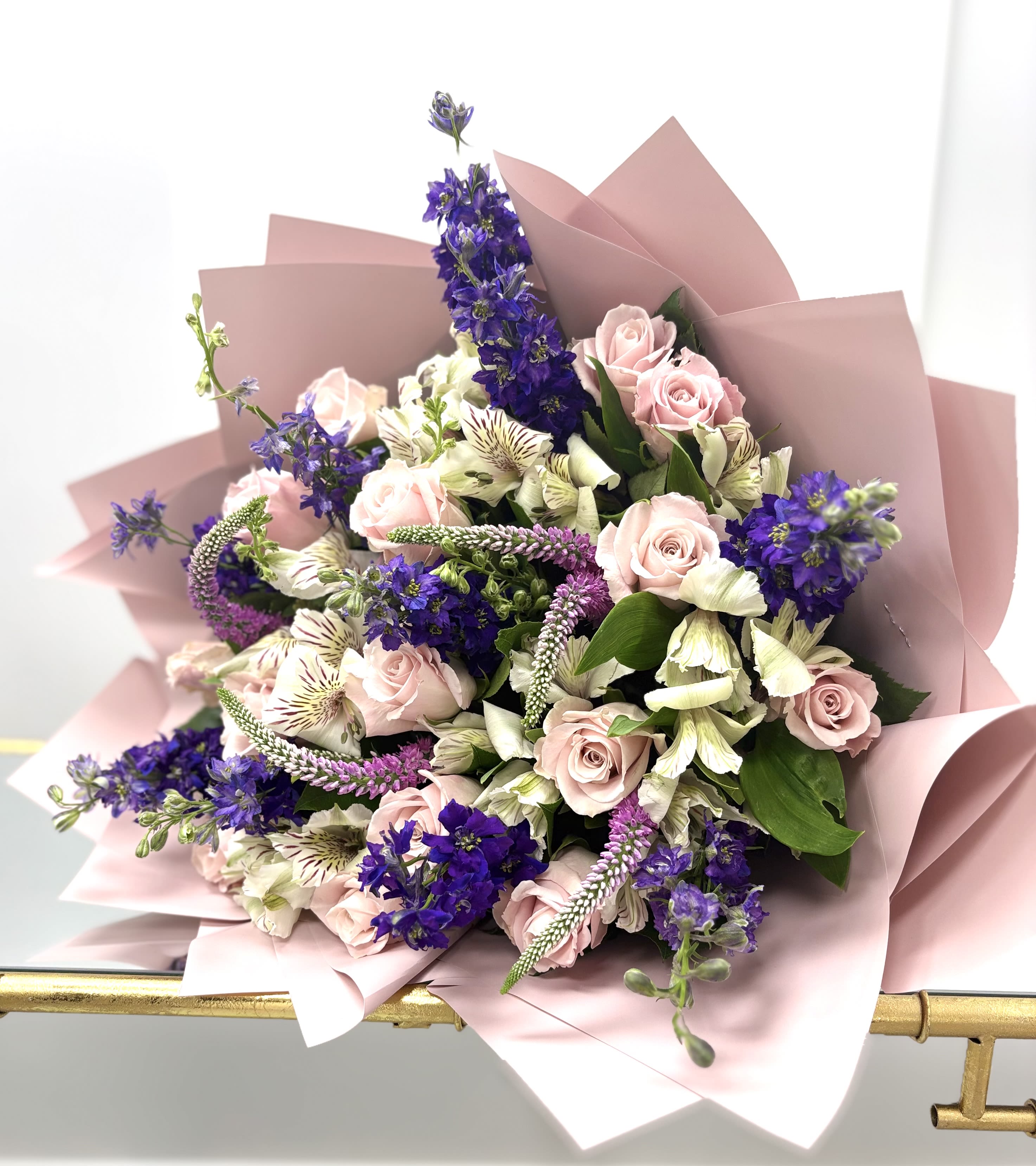 Bouquet of pink roses, purple flowers, and white blooms wrapped in blush paper