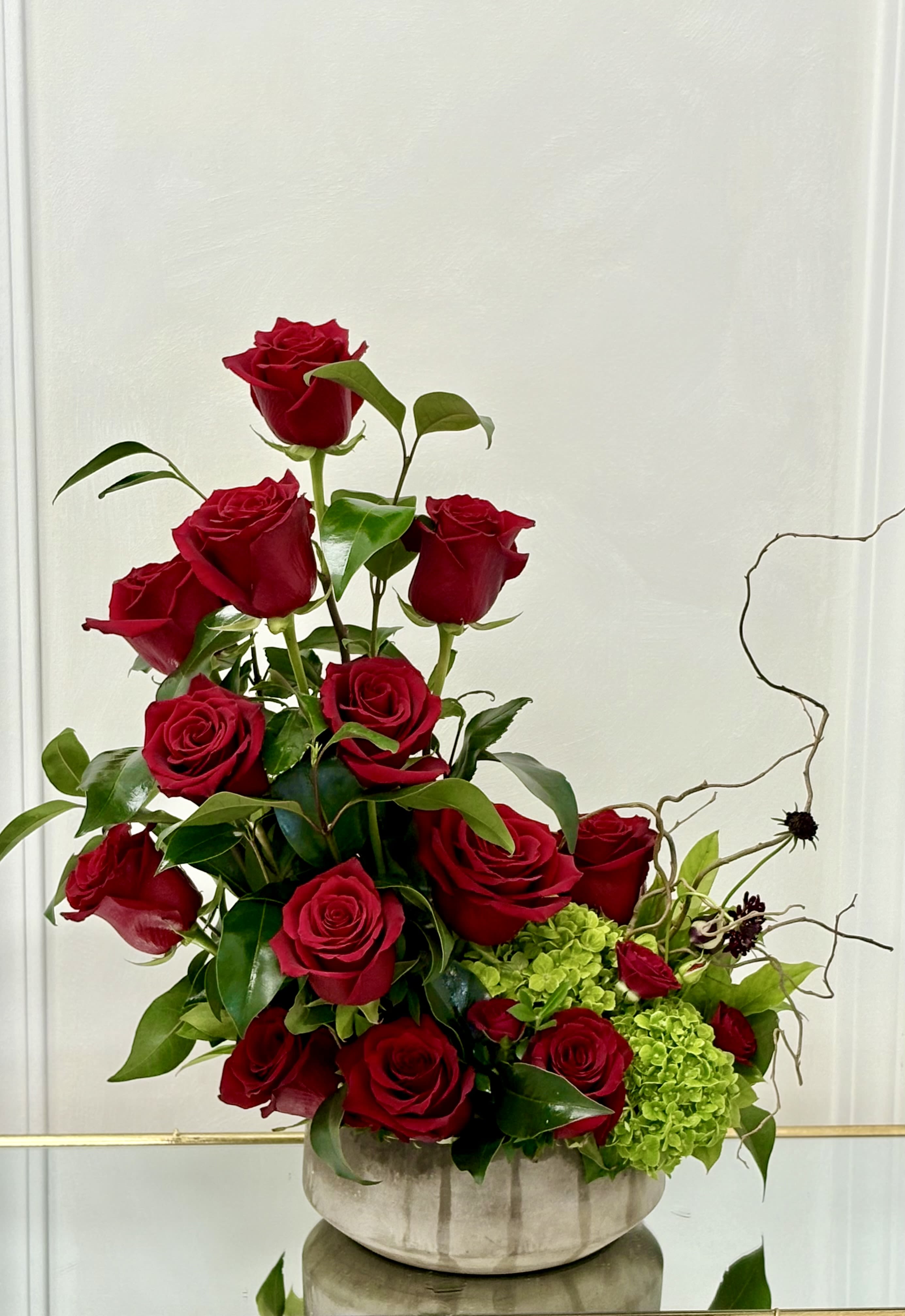 Red roses arranged in a low gray vase with green hydrangeas