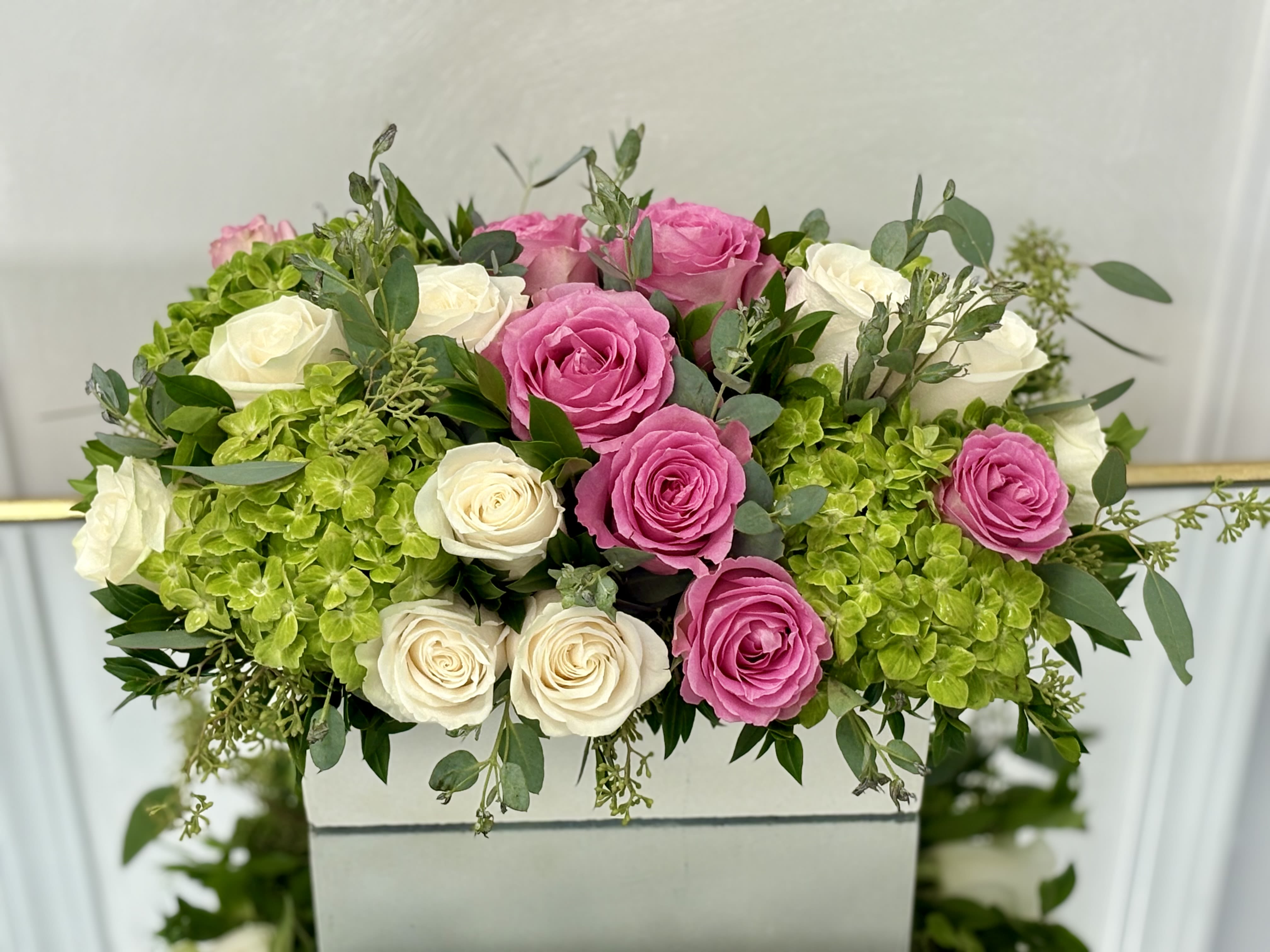 Pink and white roses arranged with green hydrangeas in a white box