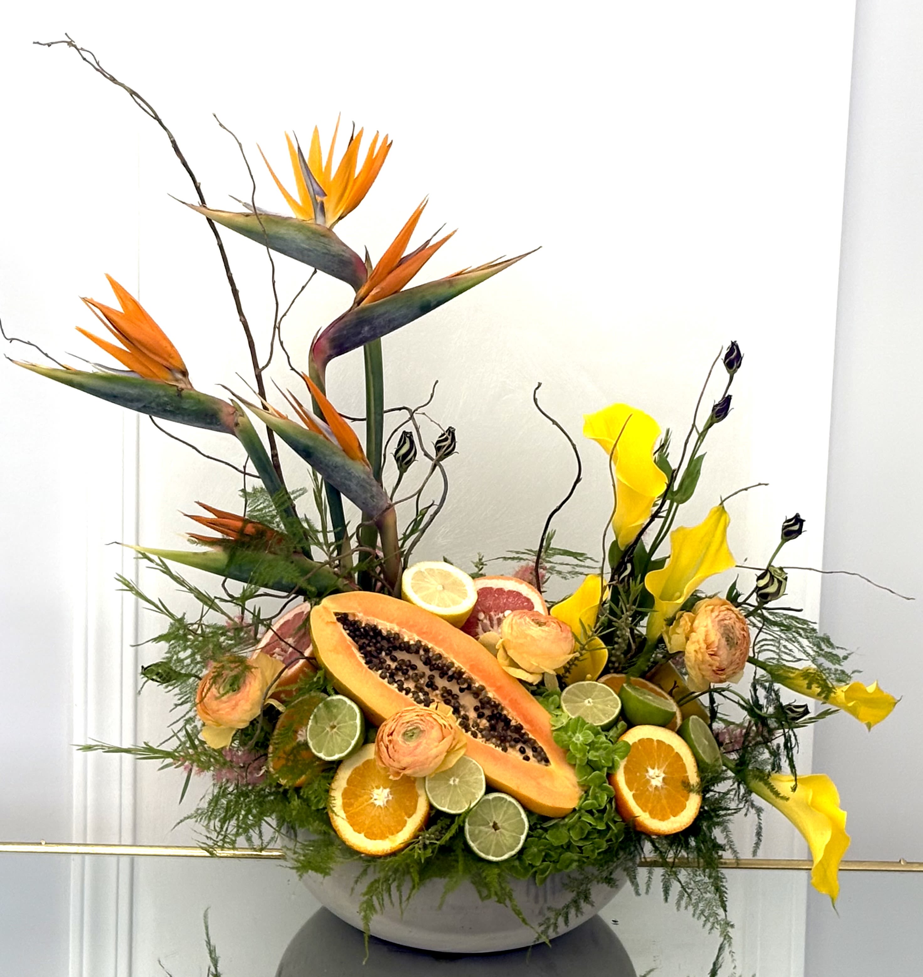 Tropical floral arrangement with bird of paradise, calla lilies, and sliced fruit in a bowl