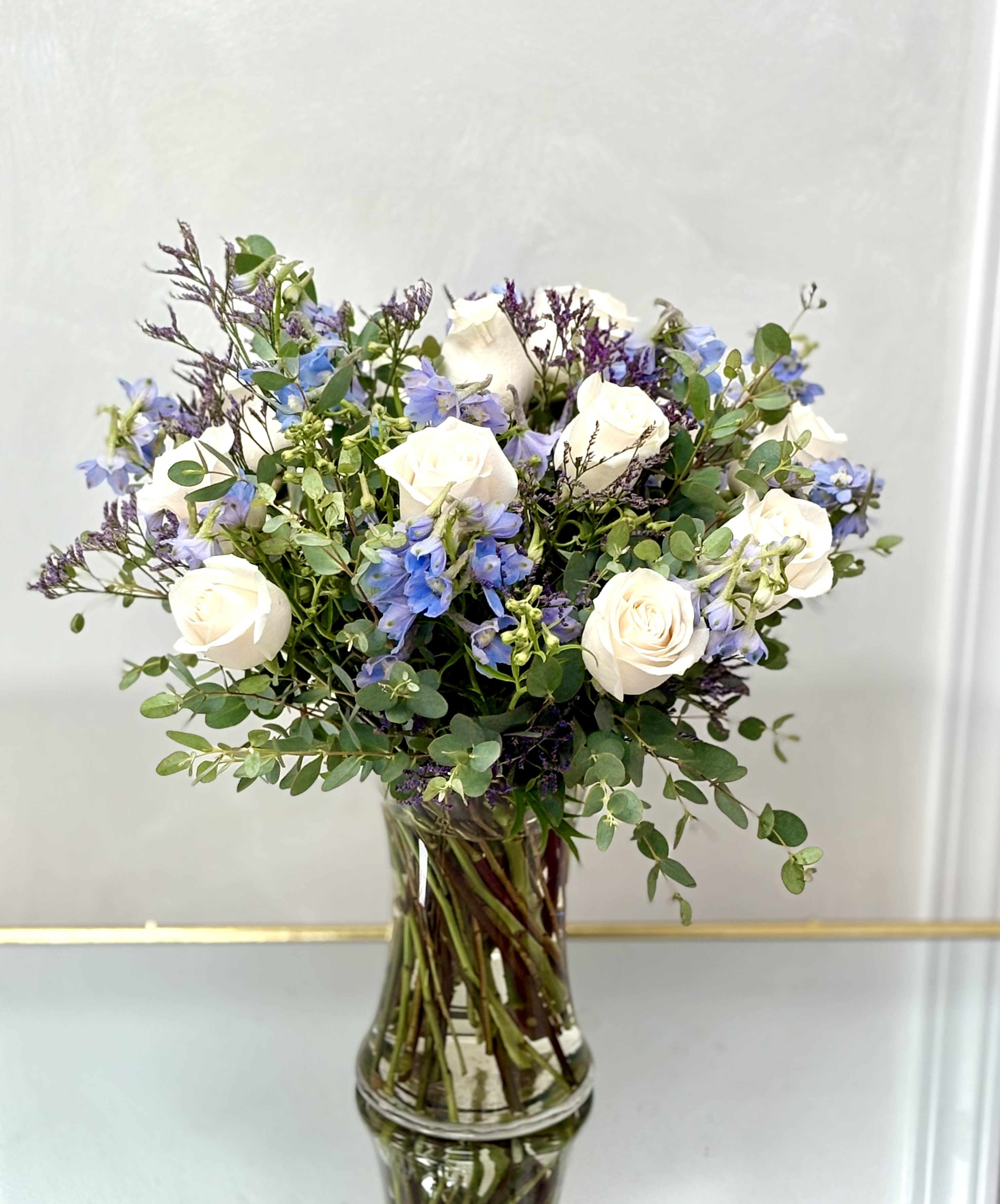 White roses and blue flowers in a clear glass vase
